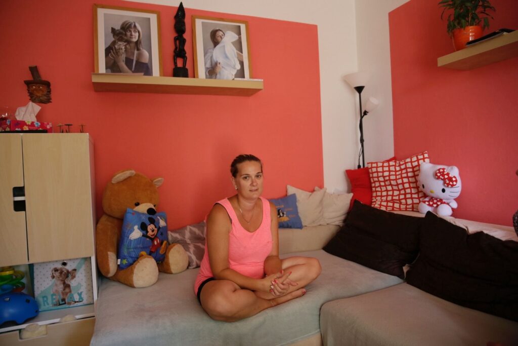 Tereza sitting cross-legged on a bed in front of a coral colored wall
